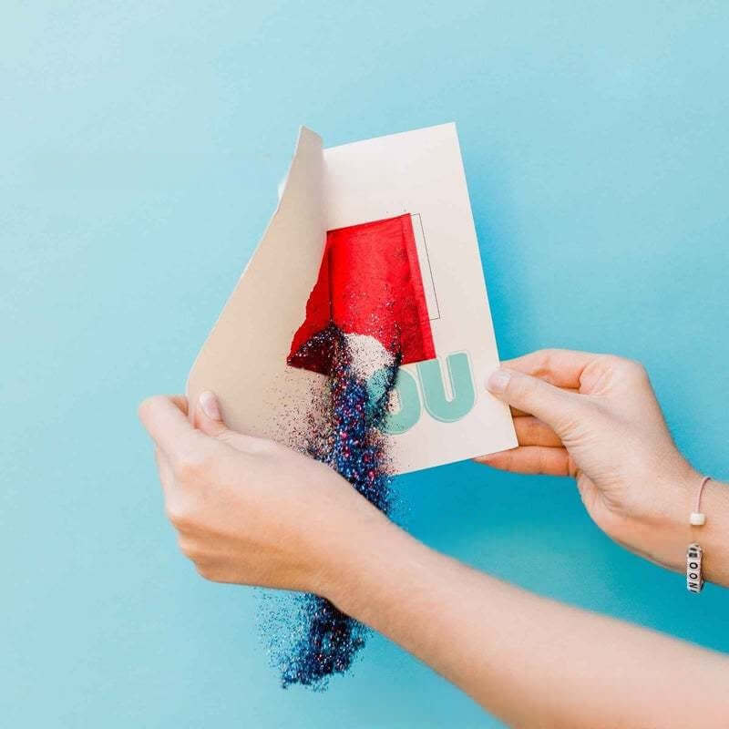 Hands opening a glitter bomb prank card with sparkly confetti spilling out, perfect for a funny birthday surprise.