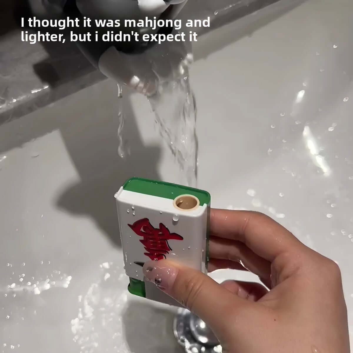 A hand holding a prank toy resembling a mahjong set while water sprays from a faucet, capturing a funny surprise moment.